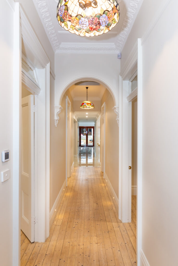 A white hallway with a wooden floor and a chandelier