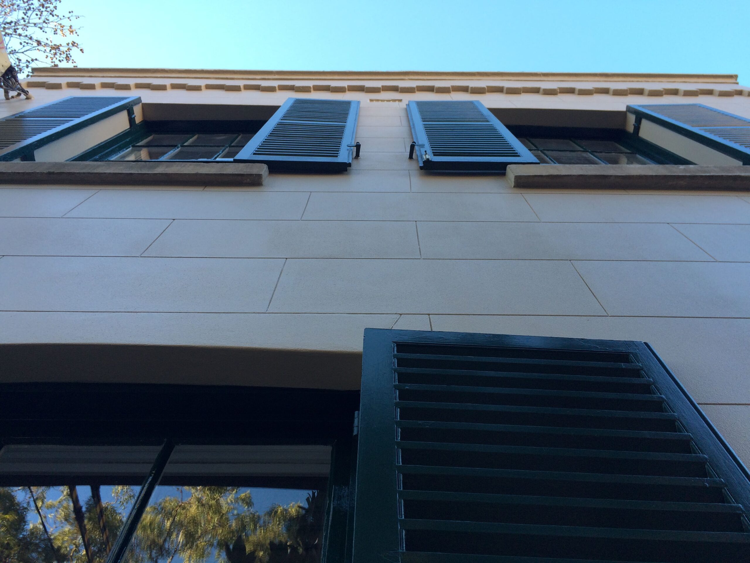 A front close view of white remedial building with windows, shutters, and blue sky