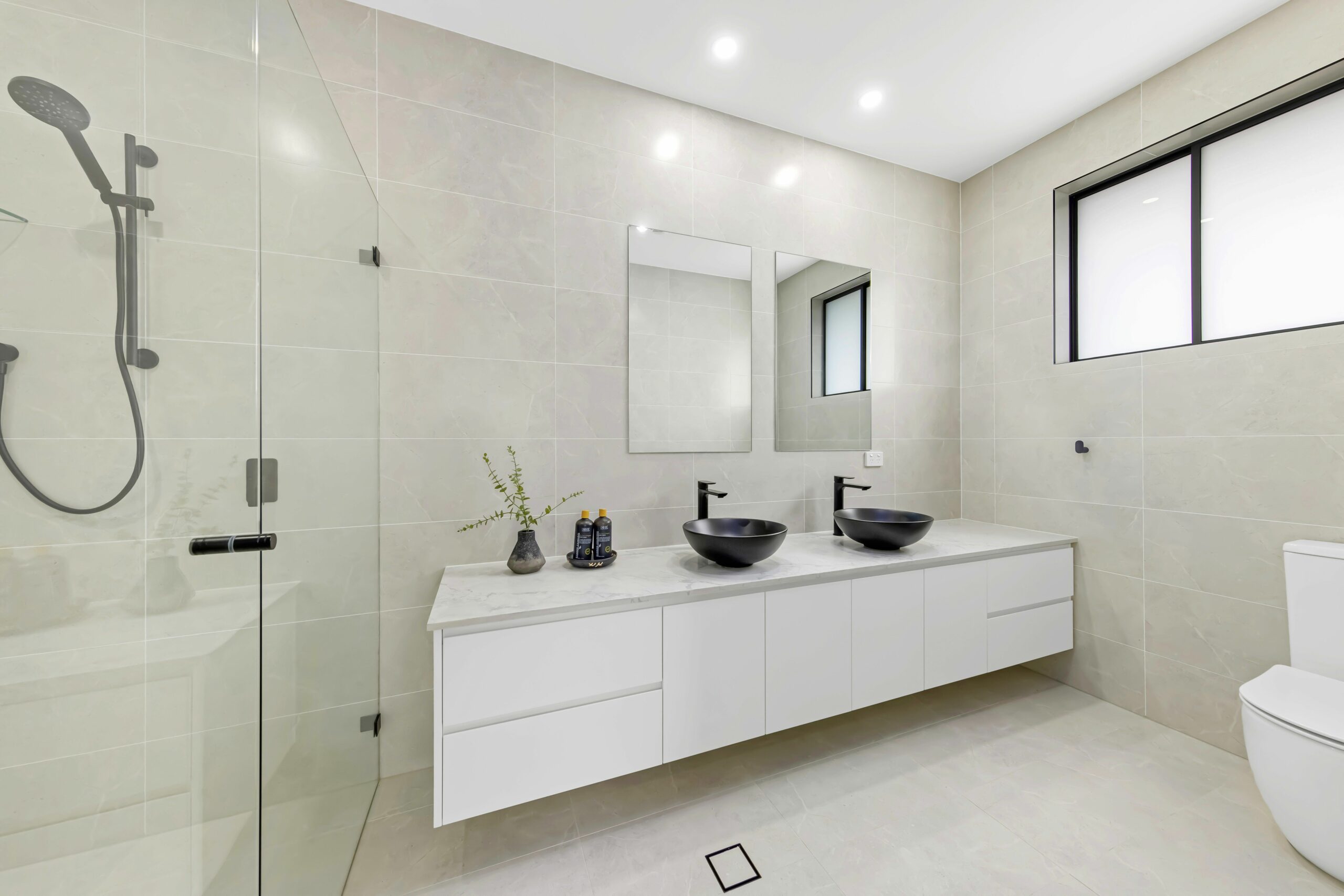 Sustainable bathroom with glass shower, two mirrors and black sinks